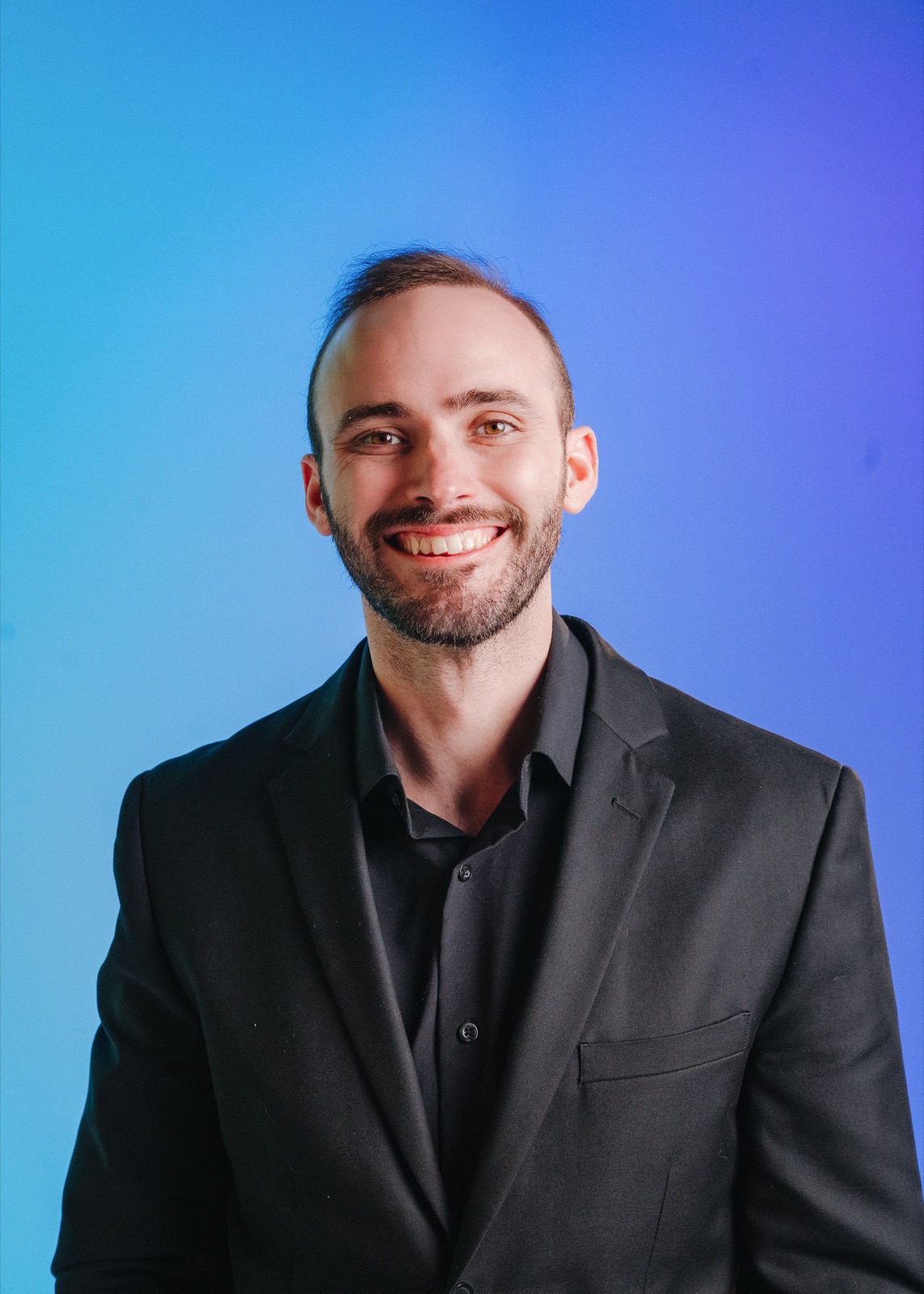 A smiling Vince K in a black blazer against blue and purple studio lighting