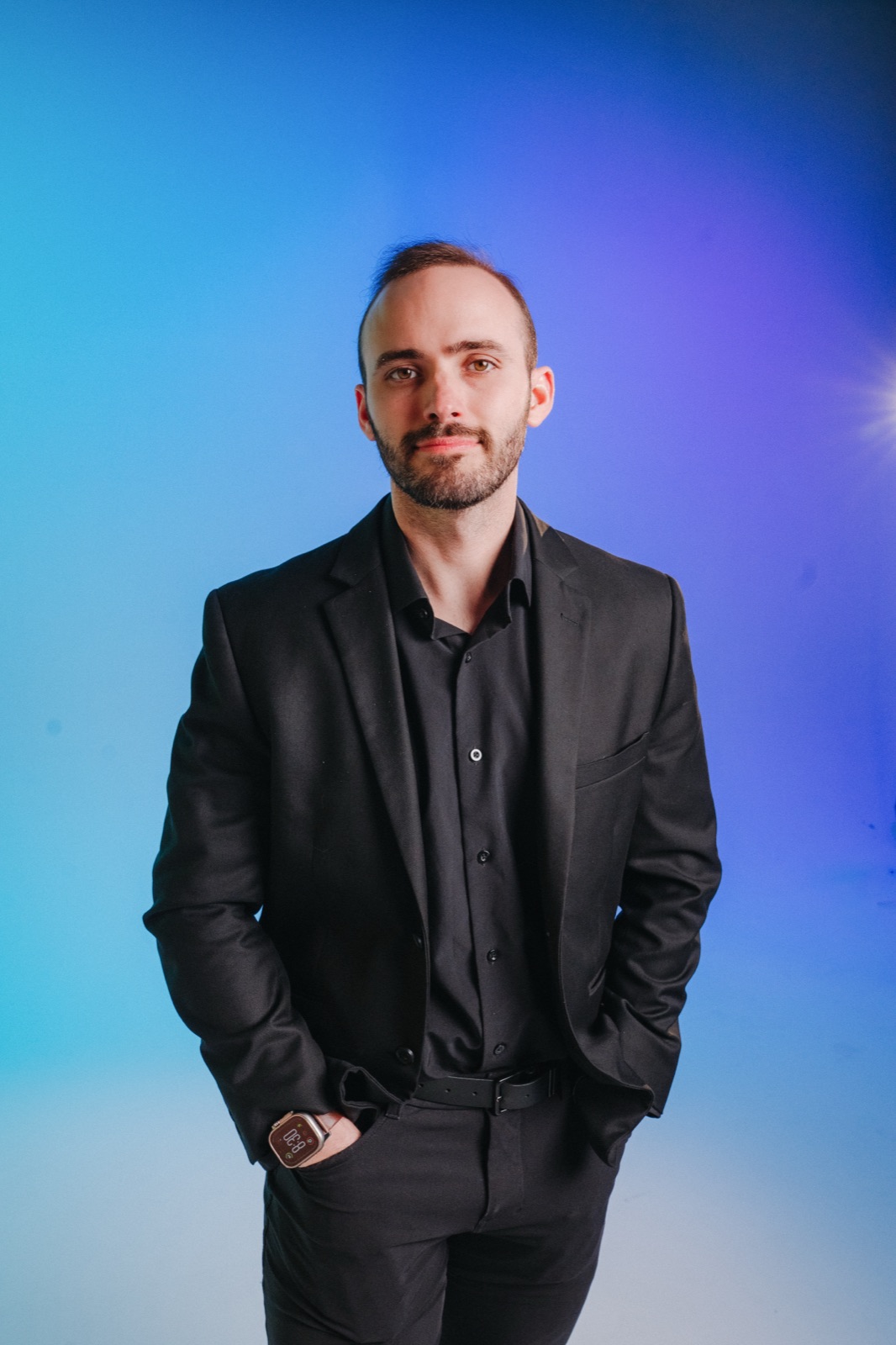 Vince K in a black suit, photographed against blue and purple studio lighting