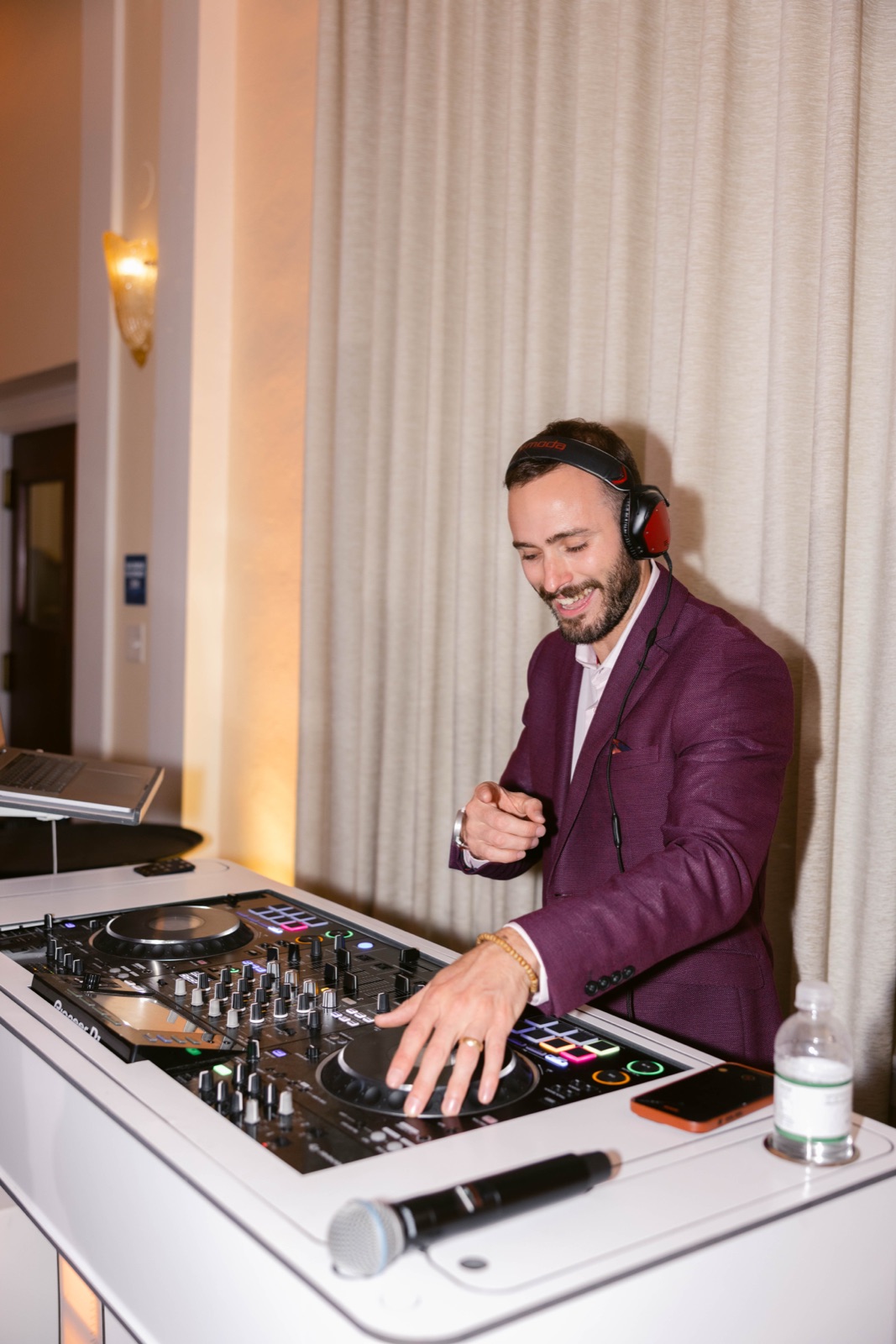 Vince K smiling while live mixing in a plum blazer and headphones